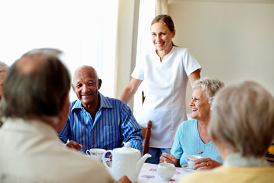 Elderly people with nurse around dining table.